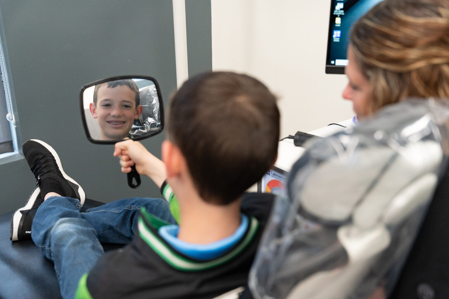 Young male patient looking at his new metal braces in a handheld mirror at Lakewood Orthodontics in Lee's Summit, MO